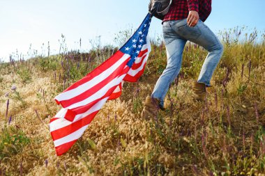 4 Temmuz. 4 Temmuz. Ulusal bayrağı olan Amerikalı. Amerikan bayrağı. Bağımsızlık günü. Vatanseverlik tatili. Adam şapka, sırt çantası, gömlek ve kot giyiyor. Güzel günbatımı ışık. 