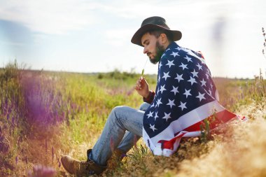 4 Temmuz. 4 Temmuz. Ulusal bayrağı olan Amerikalı. Amerikan bayrağı. Bağımsızlık günü. Vatanseverlik tatili. Adam şapka, sırt çantası, gömlek ve kot giyiyor. Güzel günbatımı ışık. 