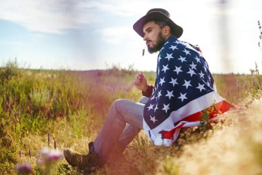 4 Temmuz. 4 Temmuz. Ulusal bayrağı olan Amerikalı. Amerikan bayrağı. Bağımsızlık günü. Vatanseverlik tatili. Adam şapka, sırt çantası, gömlek ve kot giyiyor. Güzel günbatımı ışık. 