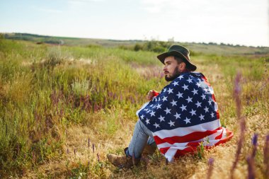 4 Temmuz. 4 Temmuz. Ulusal bayrağı olan Amerikalı. Amerikan bayrağı. Bağımsızlık günü. Vatanseverlik tatili. Adam şapka, sırt çantası, gömlek ve kot giyiyor. Güzel günbatımı ışık. 