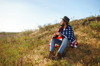 4 Temmuz. 4 Temmuz. Ulusal bayrağı olan Amerikalı. Amerikan bayrağı. Bağımsızlık günü. Vatanseverlik tatili. Adam şapka, sırt çantası, gömlek ve kot giyiyor. Güzel günbatımı ışık. 