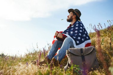 4 Temmuz. 4 Temmuz. Ulusal bayrağı olan Amerikalı. Amerikan bayrağı. Bağımsızlık günü. Vatanseverlik tatili. Adam şapka, sırt çantası, gömlek ve kot giyiyor. Güzel günbatımı ışık. 