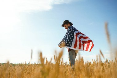 4 Temmuz. 4 Temmuz. Ulusal bayrağı olan Amerikalı. Amerikan bayrağı. Bağımsızlık günü. Vatanseverlik tatili. Adam şapka, sırt çantası, gömlek ve kot giyiyor. Güzel günbatımı ışık. 