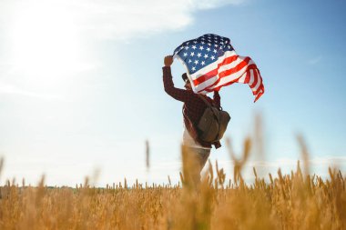 4 Temmuz. 4 Temmuz. Ulusal bayrağı olan Amerikalı. Amerikan bayrağı. Bağımsızlık günü. Vatanseverlik tatili. Adam şapka, sırt çantası, gömlek ve kot giyiyor. Güzel günbatımı ışık. 
