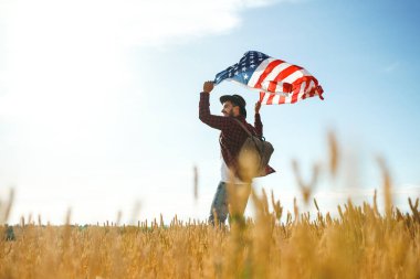 4 Temmuz. 4 Temmuz. Ulusal bayrağı olan Amerikalı. Amerikan bayrağı. Bağımsızlık günü. Vatanseverlik tatili. Adam şapka, sırt çantası, gömlek ve kot giyiyor. Güzel günbatımı ışık. 
