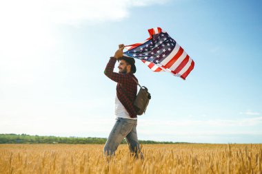 4 Temmuz. 4 Temmuz. Ulusal bayrağı olan Amerikalı. Amerikan bayrağı. Bağımsızlık günü. Vatanseverlik tatili. Adam şapka, sırt çantası, gömlek ve kot giyiyor. Güzel günbatımı ışık. 