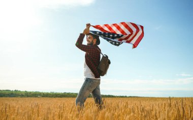 4 Temmuz. 4 Temmuz. Ulusal bayrağı olan Amerikalı. Amerikan bayrağı. Bağımsızlık günü. Vatanseverlik tatili. Adam şapka, sırt çantası, gömlek ve kot giyiyor. Güzel günbatımı ışık. 