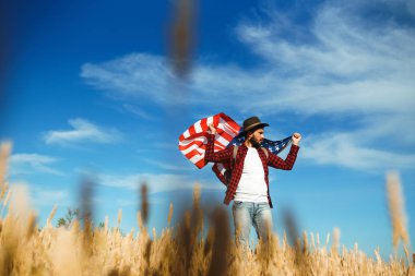 4 Temmuz. 4 Temmuz. Ulusal bayrağı olan Amerikalı. Amerikan bayrağı. Bağımsızlık günü. Vatanseverlik tatili. Adam şapka, sırt çantası, gömlek ve kot giyiyor. Güzel günbatımı ışık. 