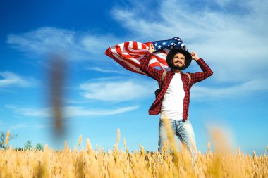 4 Temmuz. 4 Temmuz. Ulusal bayrağı olan Amerikalı. Amerikan bayrağı. Bağımsızlık günü. Vatanseverlik tatili. Adam şapka, sırt çantası, gömlek ve kot giyiyor. Güzel günbatımı ışık. 