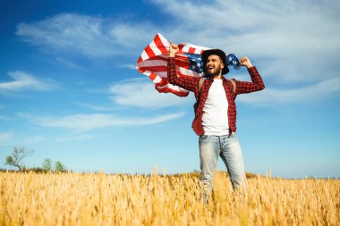 4 Temmuz. 4 Temmuz. Ulusal bayrağı olan Amerikalı. Amerikan bayrağı. Bağımsızlık günü. Vatanseverlik tatili. Adam şapka, sırt çantası, gömlek ve kot giyiyor. Güzel günbatımı ışık. 