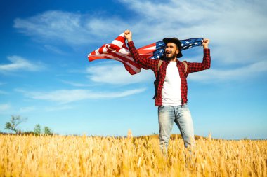 4 Temmuz. 4 Temmuz. Ulusal bayrağı olan Amerikalı. Amerikan bayrağı. Bağımsızlık günü. Vatanseverlik tatili. Adam şapka, sırt çantası, gömlek ve kot giyiyor. Güzel günbatımı ışık. 