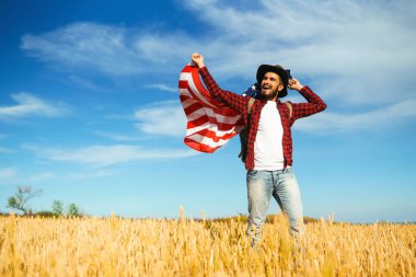 4 Temmuz. 4 Temmuz. Ulusal bayrağı olan Amerikalı. Amerikan bayrağı. Bağımsızlık günü. Vatanseverlik tatili. Adam şapka, sırt çantası, gömlek ve kot giyiyor. Güzel günbatımı ışık. 