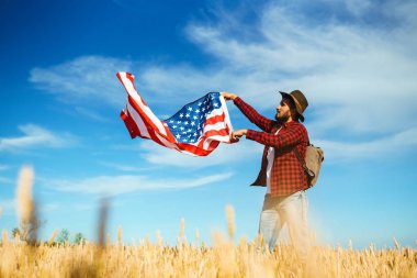4 Temmuz. 4 Temmuz. Ulusal bayrağı olan Amerikalı. Amerikan bayrağı. Bağımsızlık günü. Vatanseverlik tatili. Adam şapka, sırt çantası, gömlek ve kot giyiyor. Güzel günbatımı ışık. 
