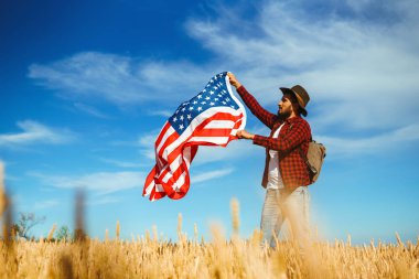 4 Temmuz. 4 Temmuz. Ulusal bayrağı olan Amerikalı. Amerikan bayrağı. Bağımsızlık günü. Vatanseverlik tatili. Adam şapka, sırt çantası, gömlek ve kot giyiyor. Güzel günbatımı ışık. 