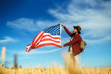 4 Temmuz. 4 Temmuz. Ulusal bayrağı olan Amerikalı. Amerikan bayrağı. Bağımsızlık günü. Vatanseverlik tatili. Adam şapka, sırt çantası, gömlek ve kot giyiyor. Güzel günbatımı ışık. 