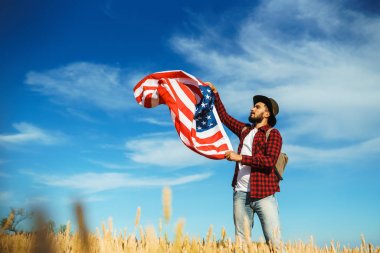 4 Temmuz. 4 Temmuz. Ulusal bayrağı olan Amerikalı. Amerikan bayrağı. Bağımsızlık günü. Vatanseverlik tatili. Adam şapka, sırt çantası, gömlek ve kot giyiyor. Güzel günbatımı ışık. 