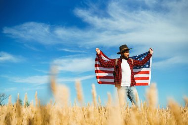 4 Temmuz. 4 Temmuz. Ulusal bayrağı olan Amerikalı. Amerikan bayrağı. Bağımsızlık günü. Vatanseverlik tatili. Adam şapka, sırt çantası, gömlek ve kot giyiyor. Güzel günbatımı ışık. 