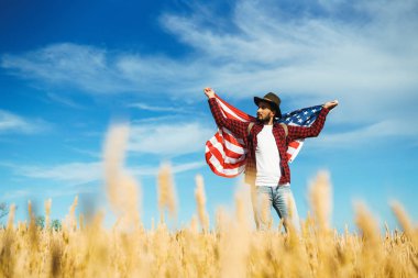 4 Temmuz. 4 Temmuz. Ulusal bayrağı olan Amerikalı. Amerikan bayrağı. Bağımsızlık günü. Vatanseverlik tatili. Adam şapka, sırt çantası, gömlek ve kot giyiyor. Güzel günbatımı ışık. 