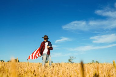 4 Temmuz. 4 Temmuz. Ulusal bayrağı olan Amerikalı. Amerikan bayrağı. Bağımsızlık günü. Vatanseverlik tatili. Adam şapka, sırt çantası, gömlek ve kot giyiyor. Güzel günbatımı ışık. 