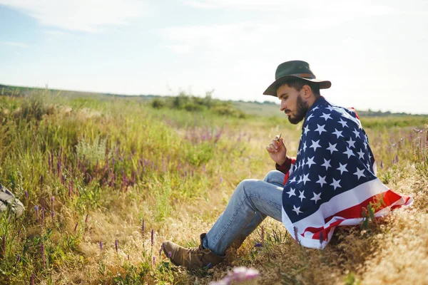 4 Temmuz. 4 Temmuz. Ulusal bayrağı olan Amerikalı. Amerikan bayrağı. Bağımsızlık günü. Vatanseverlik tatili. Adam şapka, sırt çantası, gömlek ve kot giyiyor. Güzel günbatımı ışık. 