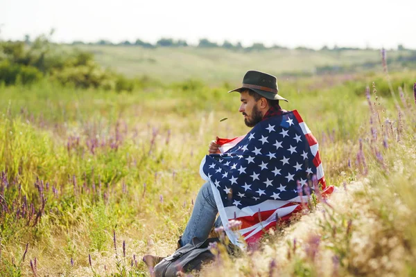 4 Temmuz. 4 Temmuz. Ulusal bayrağı olan Amerikalı. Amerikan bayrağı. Bağımsızlık günü. Vatanseverlik tatili. Adam şapka, sırt çantası, gömlek ve kot giyiyor. Güzel günbatımı ışık. 