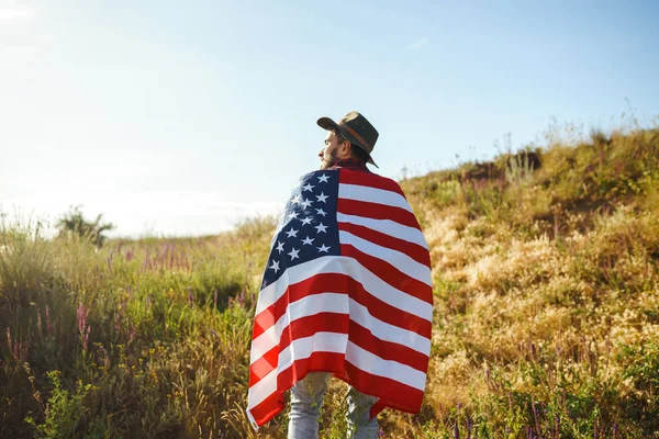4 Temmuz. 4 Temmuz. Ulusal bayrağı olan Amerikalı. Amerikan bayrağı. Bağımsızlık günü. Vatanseverlik tatili. Adam şapka, sırt çantası, gömlek ve kot giyiyor. Güzel günbatımı ışık. 