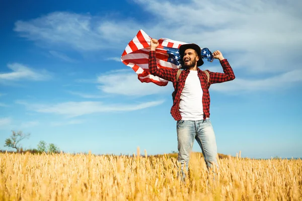 4 Temmuz. 4 Temmuz. Ulusal bayrağı olan Amerikalı. Amerikan bayrağı. Bağımsızlık günü. Vatanseverlik tatili. Adam şapka, sırt çantası, gömlek ve kot giyiyor. Güzel günbatımı ışık. 