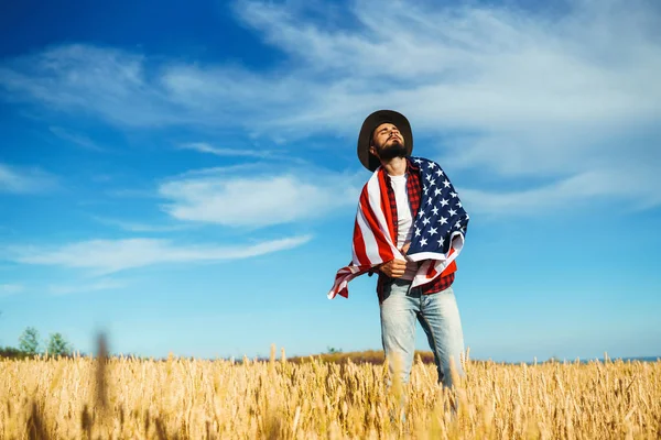 4 Temmuz. 4 Temmuz. Ulusal bayrağı olan Amerikalı. Amerikan bayrağı. Bağımsızlık günü. Vatanseverlik tatili. Adam şapka, sırt çantası, gömlek ve kot giyiyor. Güzel günbatımı ışık. 