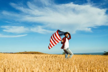 4 Temmuz. 4 Temmuz. Ulusal bayrağı olan Amerikalı. Amerikan bayrağı. Bağımsızlık günü. Vatanseverlik tatili. Adam şapka, sırt çantası, gömlek ve kot giyiyor. Güzel günbatımı ışık. 