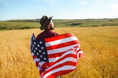 4 Temmuz. 4 Temmuz. Ulusal bayrağı olan Amerikalı. Amerikan bayrağı. Bağımsızlık günü. Vatanseverlik tatili. Adam şapka, sırt çantası, gömlek ve kot giyiyor. Güzel günbatımı ışık. 
