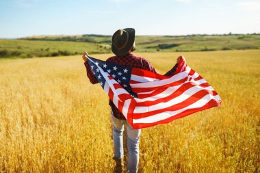 4 Temmuz. 4 Temmuz. Ulusal bayrağı olan Amerikalı. Amerikan bayrağı. Bağımsızlık günü. Vatanseverlik tatili. Adam şapka, sırt çantası, gömlek ve kot giyiyor. Güzel günbatımı ışık. 