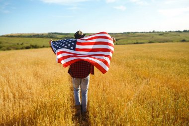4 Temmuz. 4 Temmuz. Ulusal bayrağı olan Amerikalı. Amerikan bayrağı. Bağımsızlık günü. Vatanseverlik tatili. Adam şapka, sırt çantası, gömlek ve kot giyiyor. Güzel günbatımı ışık. 
