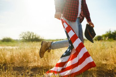 4 Temmuz. 4 Temmuz. Ulusal bayrağı olan Amerikalı. Amerikan bayrağı. Bağımsızlık günü. Vatanseverlik tatili. Adam şapka, sırt çantası, gömlek ve kot giyiyor. Güzel günbatımı ışık. 