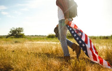 4 Temmuz. 4 Temmuz. Ulusal bayrağı olan Amerikalı. Amerikan bayrağı. Bağımsızlık günü. Vatanseverlik tatili. Adam şapka, sırt çantası, gömlek ve kot giyiyor. Güzel günbatımı ışık. 