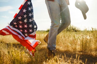 4 Temmuz. 4 Temmuz. Ulusal bayrağı olan Amerikalı. Amerikan bayrağı. Bağımsızlık günü. Vatanseverlik tatili. Adam şapka, sırt çantası, gömlek ve kot giyiyor. Güzel günbatımı ışık. 