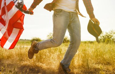 4 Temmuz. 4 Temmuz. Ulusal bayrağı olan Amerikalı. Amerikan bayrağı. Bağımsızlık günü. Vatanseverlik tatili. Adam şapka, sırt çantası, gömlek ve kot giyiyor. Güzel günbatımı ışık. 