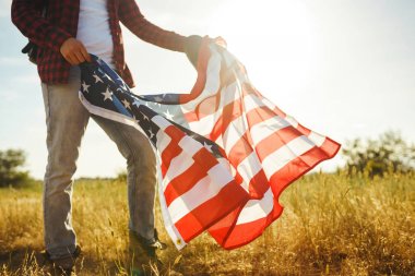 4 Temmuz. 4 Temmuz. Ulusal bayrağı olan Amerikalı. Amerikan bayrağı. Bağımsızlık günü. Vatanseverlik tatili. Adam şapka, sırt çantası, gömlek ve kot giyiyor. Güzel günbatımı ışık. 