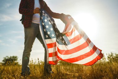 4 Temmuz. 4 Temmuz. Ulusal bayrağı olan Amerikalı. Amerikan bayrağı. Bağımsızlık günü. Vatanseverlik tatili. Adam şapka, sırt çantası, gömlek ve kot giyiyor. Güzel günbatımı ışık. 