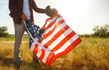 4 Temmuz. 4 Temmuz. Ulusal bayrağı olan Amerikalı. Amerikan bayrağı. Bağımsızlık günü. Vatanseverlik tatili. Adam şapka, sırt çantası, gömlek ve kot giyiyor. Güzel günbatımı ışık. 