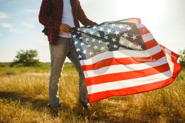 4 Temmuz. 4 Temmuz. Ulusal bayrağı olan Amerikalı. Amerikan bayrağı. Bağımsızlık günü. Vatanseverlik tatili. Adam şapka, sırt çantası, gömlek ve kot giyiyor. Güzel günbatımı ışık. 
