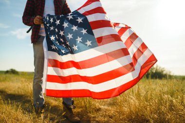 4 Temmuz. 4 Temmuz. Ulusal bayrağı olan Amerikalı. Amerikan bayrağı. Bağımsızlık günü. Vatanseverlik tatili. Adam şapka, sırt çantası, gömlek ve kot giyiyor. Güzel günbatımı ışık. 