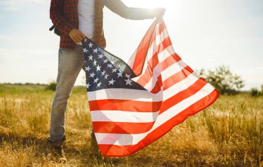 4 Temmuz. 4 Temmuz. Ulusal bayrağı olan Amerikalı. Amerikan bayrağı. Bağımsızlık günü. Vatanseverlik tatili. Adam şapka, sırt çantası, gömlek ve kot giyiyor. Güzel günbatımı ışık. 