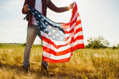 4 Temmuz. 4 Temmuz. Ulusal bayrağı olan Amerikalı. Amerikan bayrağı. Bağımsızlık günü. Vatanseverlik tatili. Adam şapka, sırt çantası, gömlek ve kot giyiyor. Güzel günbatımı ışık. 