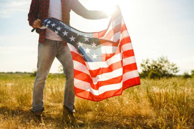 4 Temmuz. 4 Temmuz. Ulusal bayrağı olan Amerikalı. Amerikan bayrağı. Bağımsızlık günü. Vatanseverlik tatili. Adam şapka, sırt çantası, gömlek ve kot giyiyor. Güzel günbatımı ışık. 