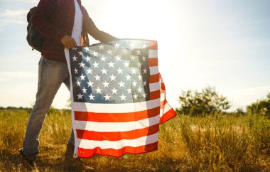 4 Temmuz. 4 Temmuz. Ulusal bayrağı olan Amerikalı. Amerikan bayrağı. Bağımsızlık günü. Vatanseverlik tatili. Adam şapka, sırt çantası, gömlek ve kot giyiyor. Güzel günbatımı ışık. 