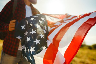 4 Temmuz. 4 Temmuz. Ulusal bayrağı olan Amerikalı. Amerikan bayrağı. Bağımsızlık günü. Vatanseverlik tatili. Adam şapka, sırt çantası, gömlek ve kot giyiyor. Güzel günbatımı ışık. 