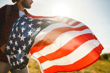 4 Temmuz. 4 Temmuz. Ulusal bayrağı olan Amerikalı. Amerikan bayrağı. Bağımsızlık günü. Vatanseverlik tatili. Adam şapka, sırt çantası, gömlek ve kot giyiyor. Güzel günbatımı ışık. 