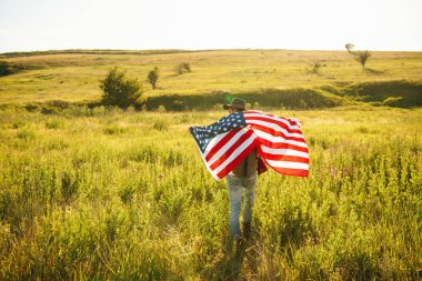 4 Temmuz. 4 Temmuz. Ulusal bayrağı olan Amerikalı. Amerikan bayrağı. Bağımsızlık günü. Vatanseverlik tatili. Adam şapka, sırt çantası, gömlek ve kot giyiyor. Güzel günbatımı ışık. 