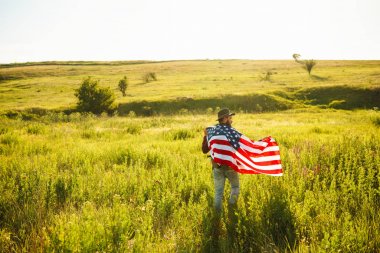 4 Temmuz. 4 Temmuz. Ulusal bayrağı olan Amerikalı. Amerikan bayrağı. Bağımsızlık günü. Vatanseverlik tatili. Adam şapka, sırt çantası, gömlek ve kot giyiyor. Güzel günbatımı ışık. 