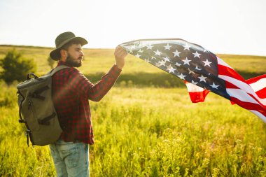 4 Temmuz. 4 Temmuz. Ulusal bayrağı olan Amerikalı. Amerikan bayrağı. Bağımsızlık günü. Vatanseverlik tatili. Adam şapka, sırt çantası, gömlek ve kot giyiyor. Güzel günbatımı ışık. 